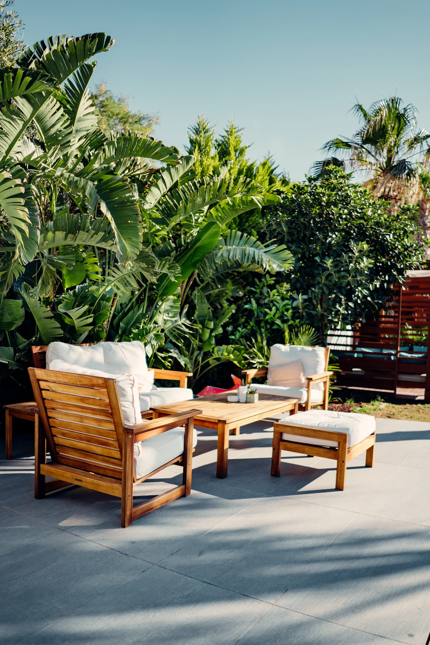 Wooden outdoor seating with white cushions among tropical plants